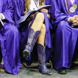 A TCU graduate wears purple cowboy boots with her commencement gown