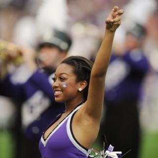 A smiling TCU Showgirl makes the two-fingered "Go Frogs" hand sign at a crowded football game.